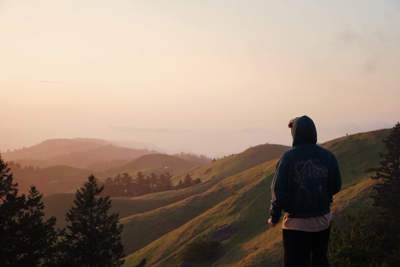 Sleeping Lady hoodie photographed on a hillside at sunset